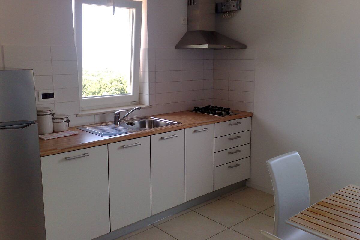 A kitchen with white cabinets, a wooden countertop, a stainless steel sink, a gas stove, and a window.
