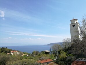 A coastal view with a prominent white tower, lush greenery, and a clear blue sea.