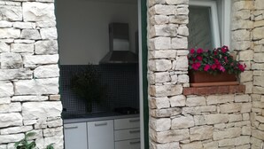 A stone exterior with a kitchen visible inside. There is a window with pink flowers and a potted plant with white flowers. - Villa Brumnic Apartments (Moscenicka Draga)