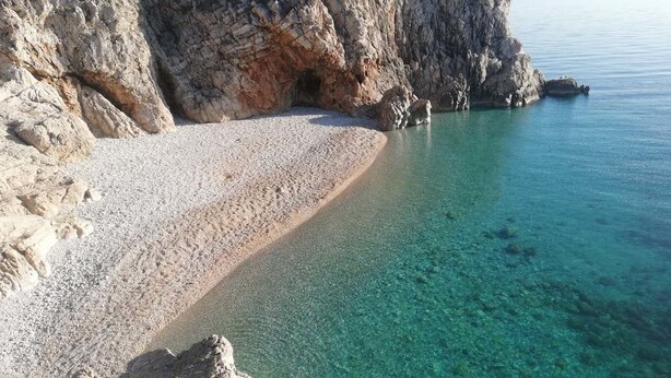 A pebble beach with clear water and rocky cliffs. - Villa Brumnic Apartments (Moscenicka Draga)