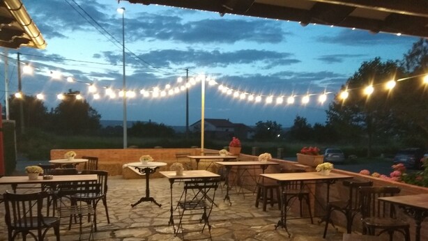 Patio esterno con pavimento in pietra, tavoli e sedie, decorato con luci a stringa.