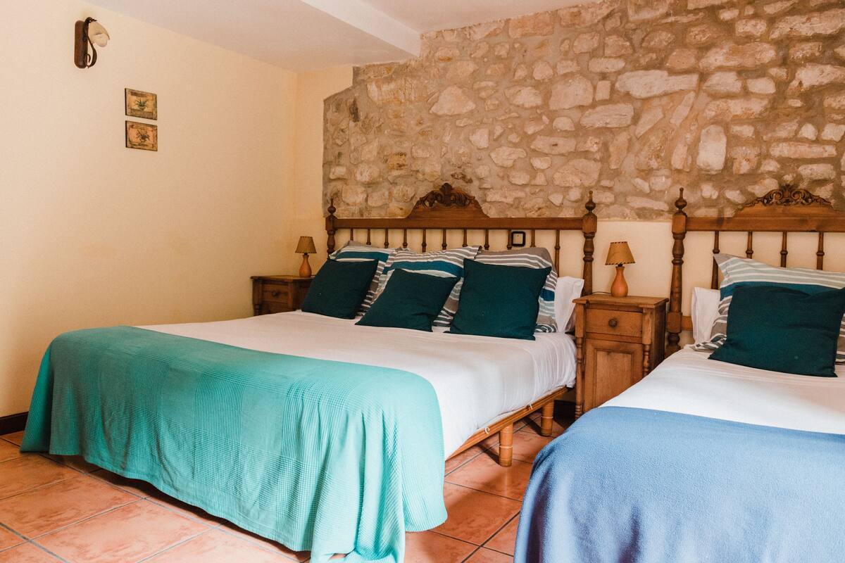 A bedroom with two beds, stone wall, wooden headboard, and tiled floor.