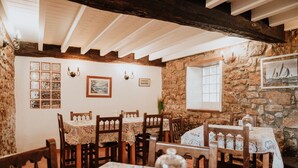 Un'accogliente sala da pranzo rustica con pareti in pietra, travi in legno e tavoli apparecchiati con tovaglie floreali.
