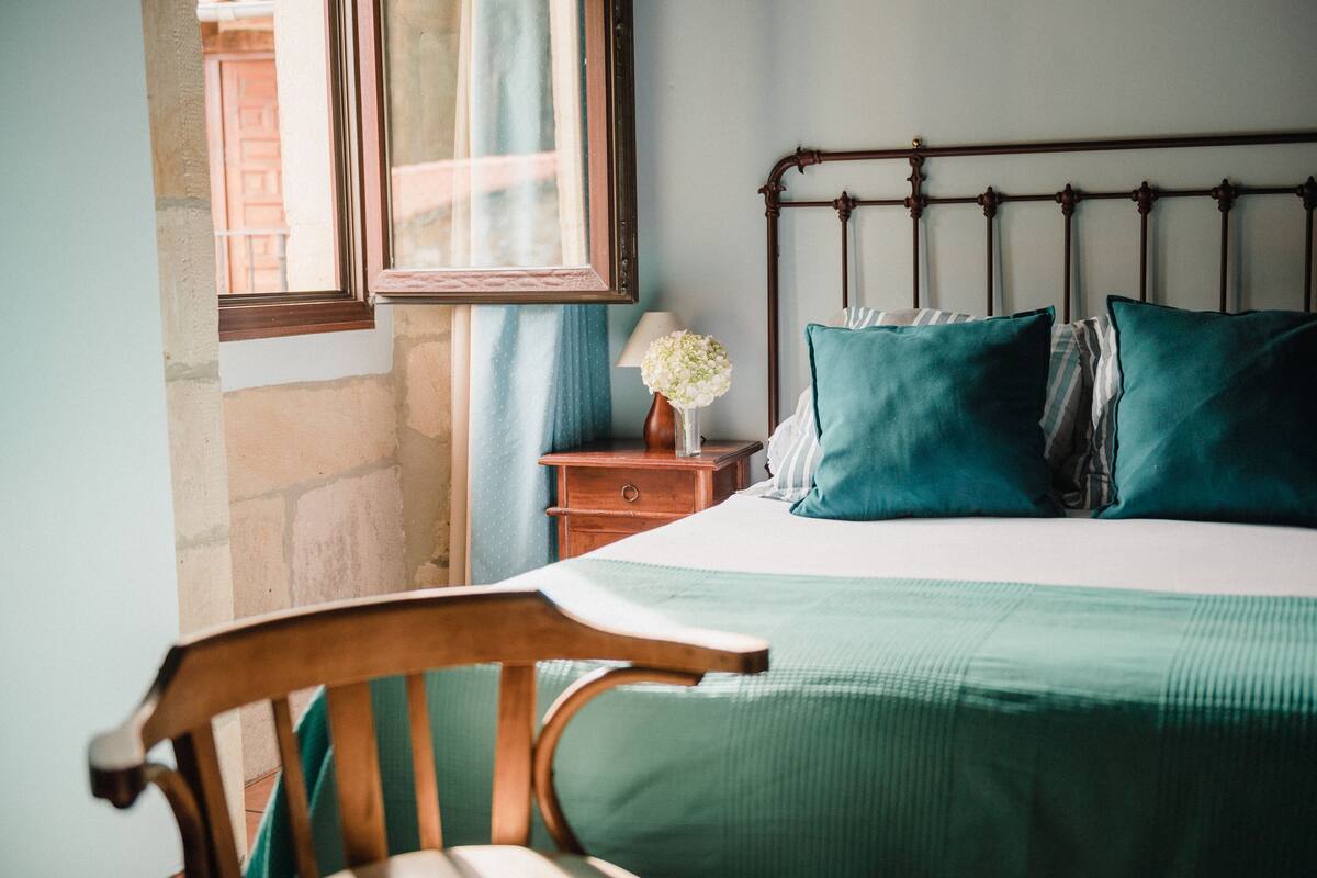 A bedroom with a wooden headboard, a green bedspread, and a nightstand with a vase of flowers.