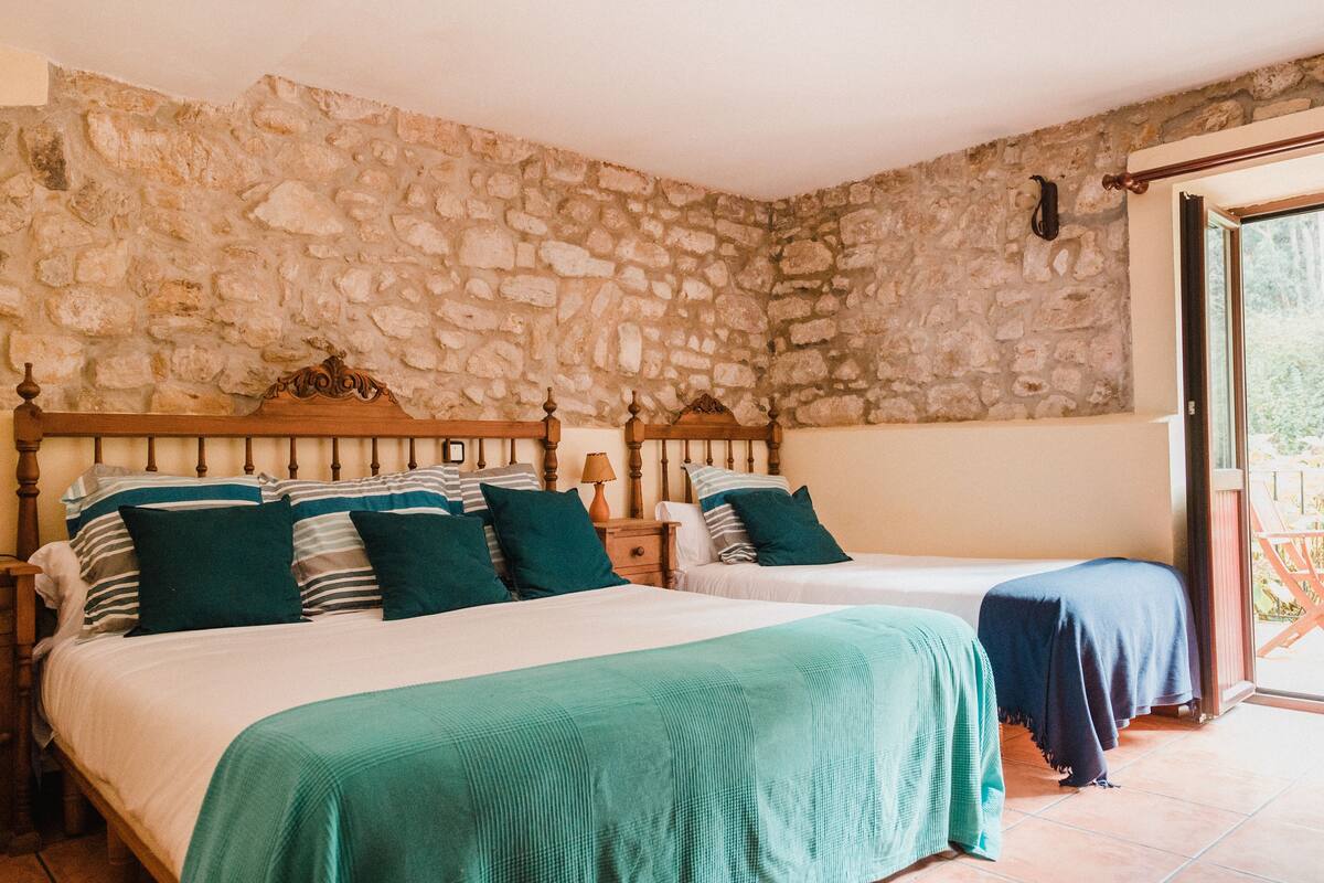 A bedroom with two beds, stone walls, and a balcony.