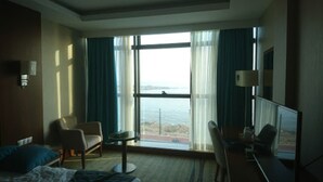 Een hotelkamer met een bed, een bureau, een stoel, een kleine tafel en een groot raam met uitzicht op zee.