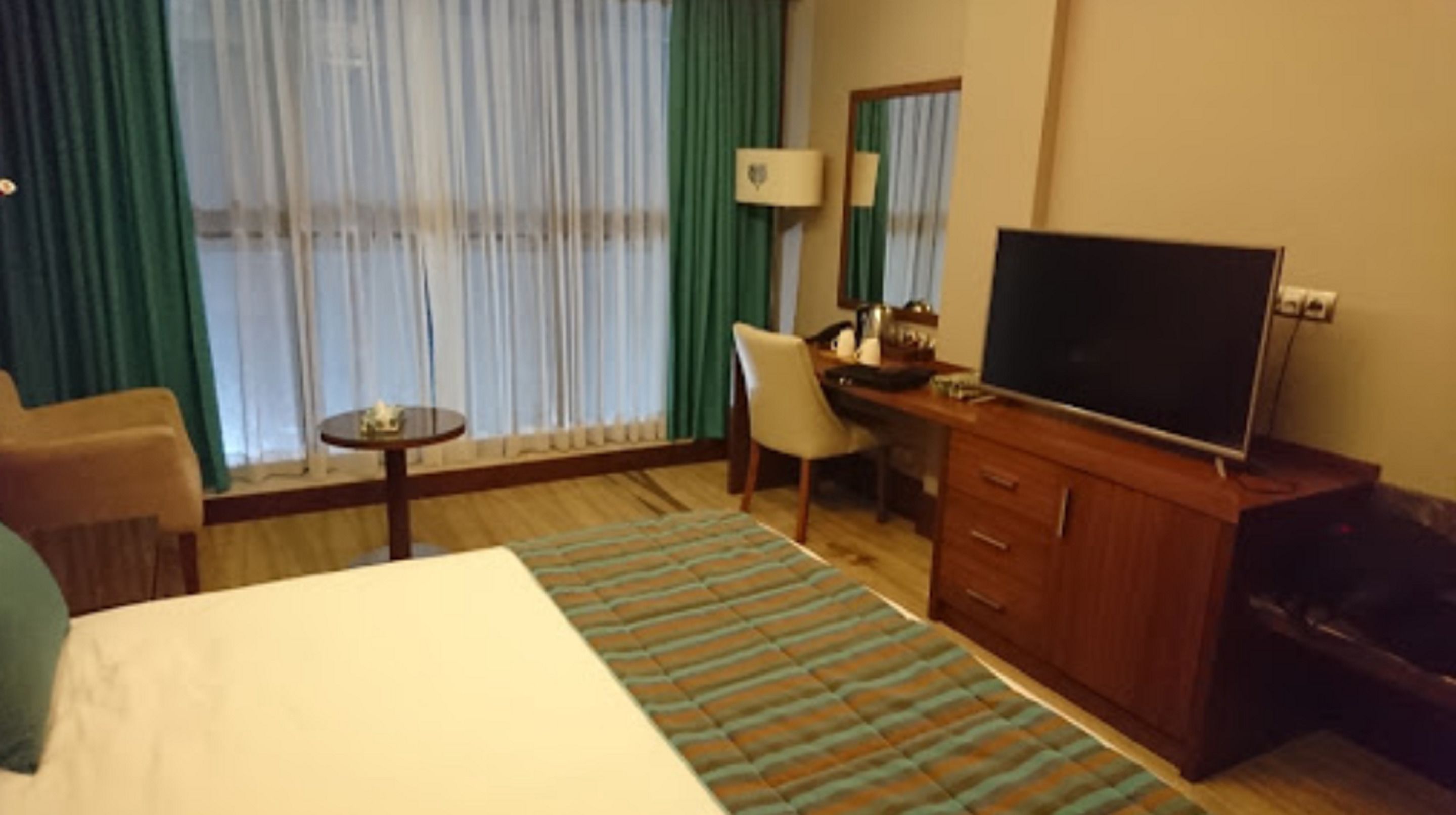 Una camera d'albergo con un letto, una scrivania, una sedia, una televisione e un tavolino.