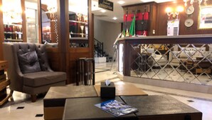 Een ontvangsthal met een leren fauteuil, een houten bijzettafeltje en een bar met een toonbank en krukken.