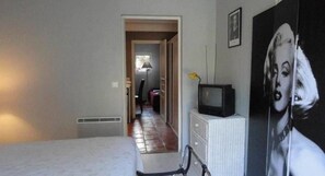 A room with a bed, a dresser, a television, and a poster on the wall. - Riad des Vignes (Ramatuelle)