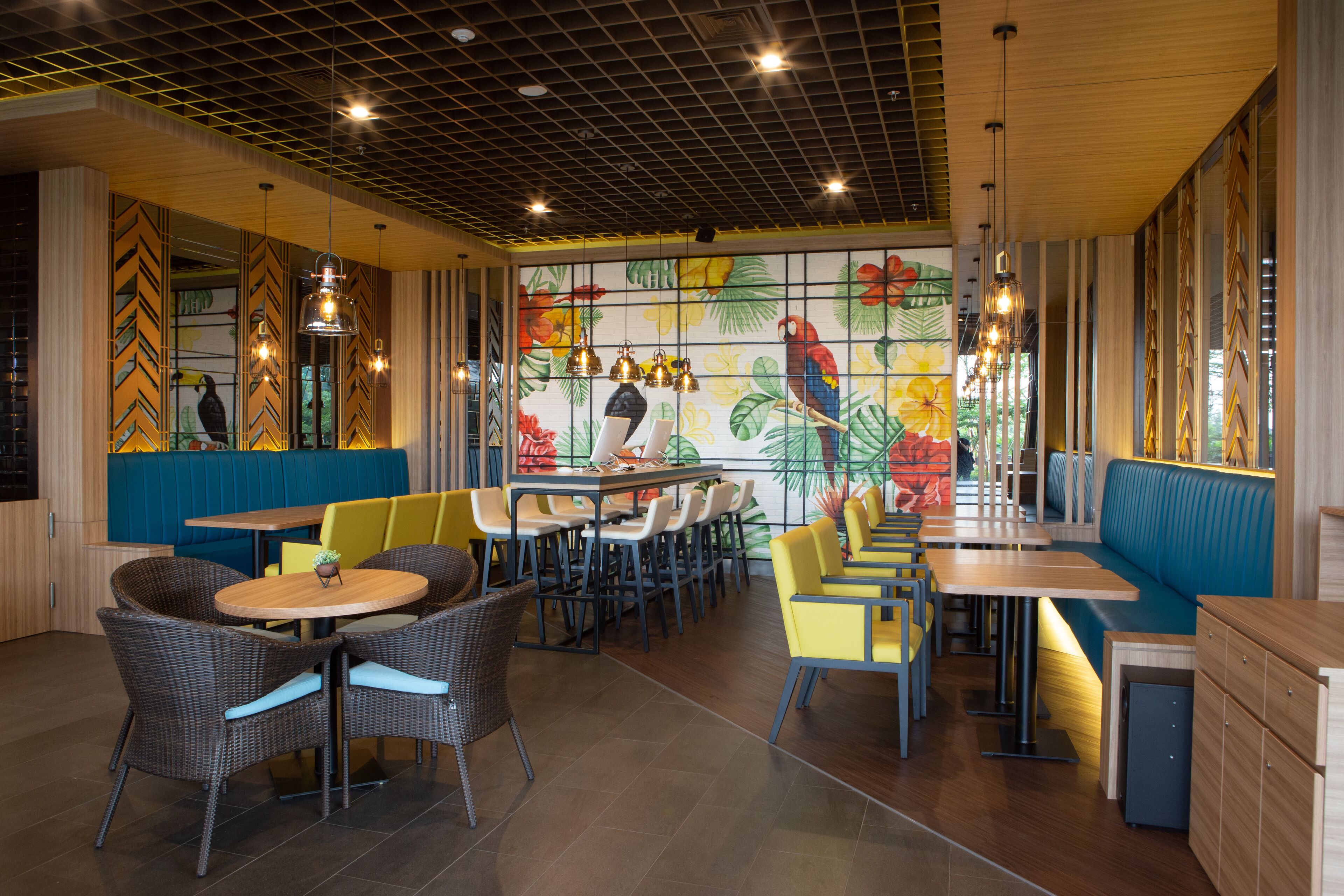 Un restaurante con cabinas y mesas, un mural con aves tropicales e iluminación colgante.