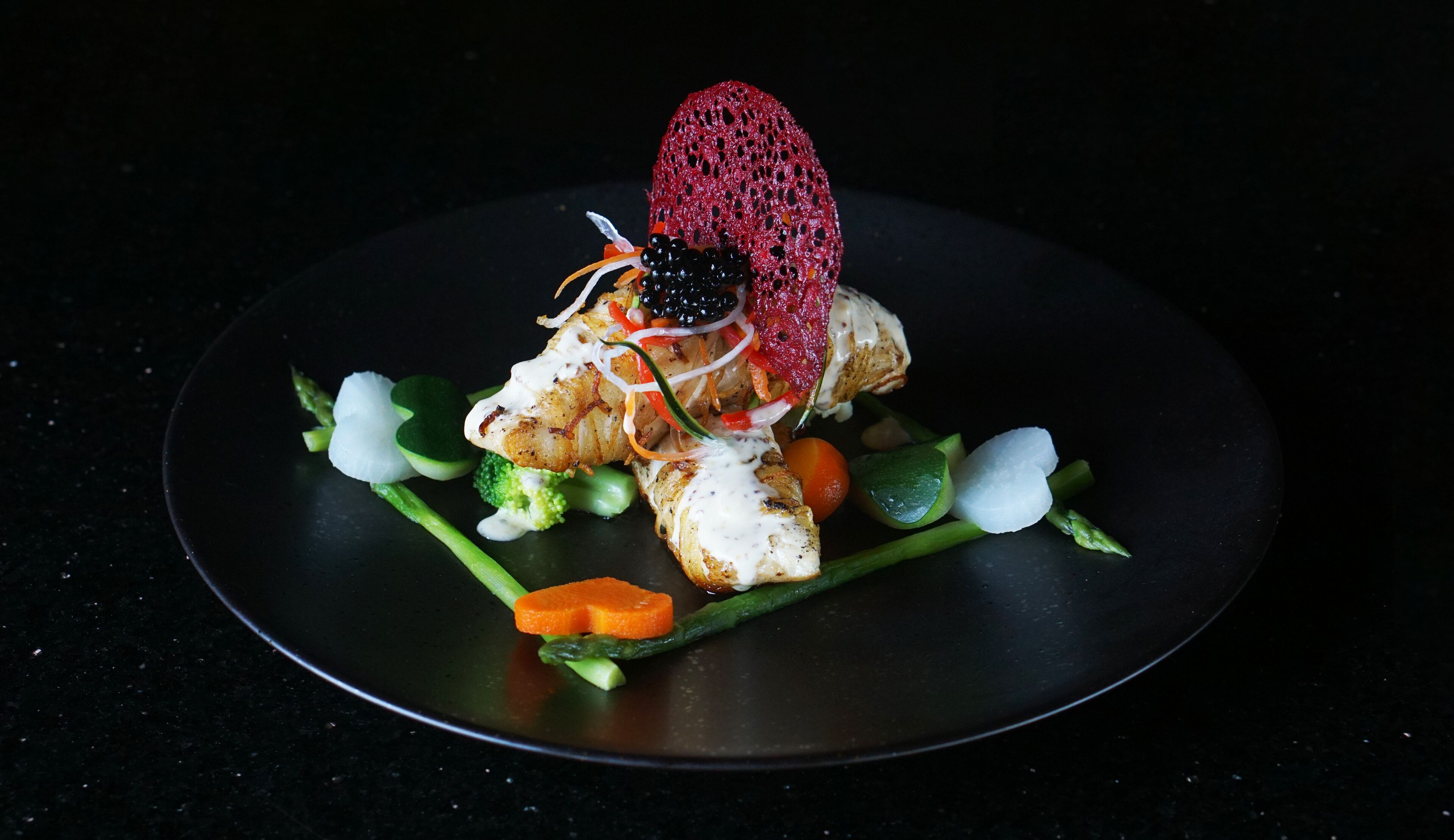 A plate of food with a variety of vegetables and a piece of meat, possibly chicken, topped with a red berry and blackberries.