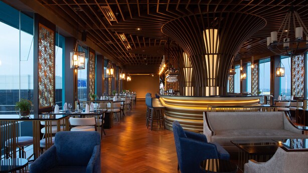 Een modern restaurantinterieur met een gebogen bar, houten vloeren en grote ramen met uitzicht op de stad.