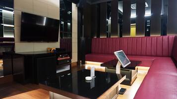 Un interior moderno con un mostrador de recepción negro, un televisor de pantalla plana, una zona de estar con cojines rojos y un suelo de madera.