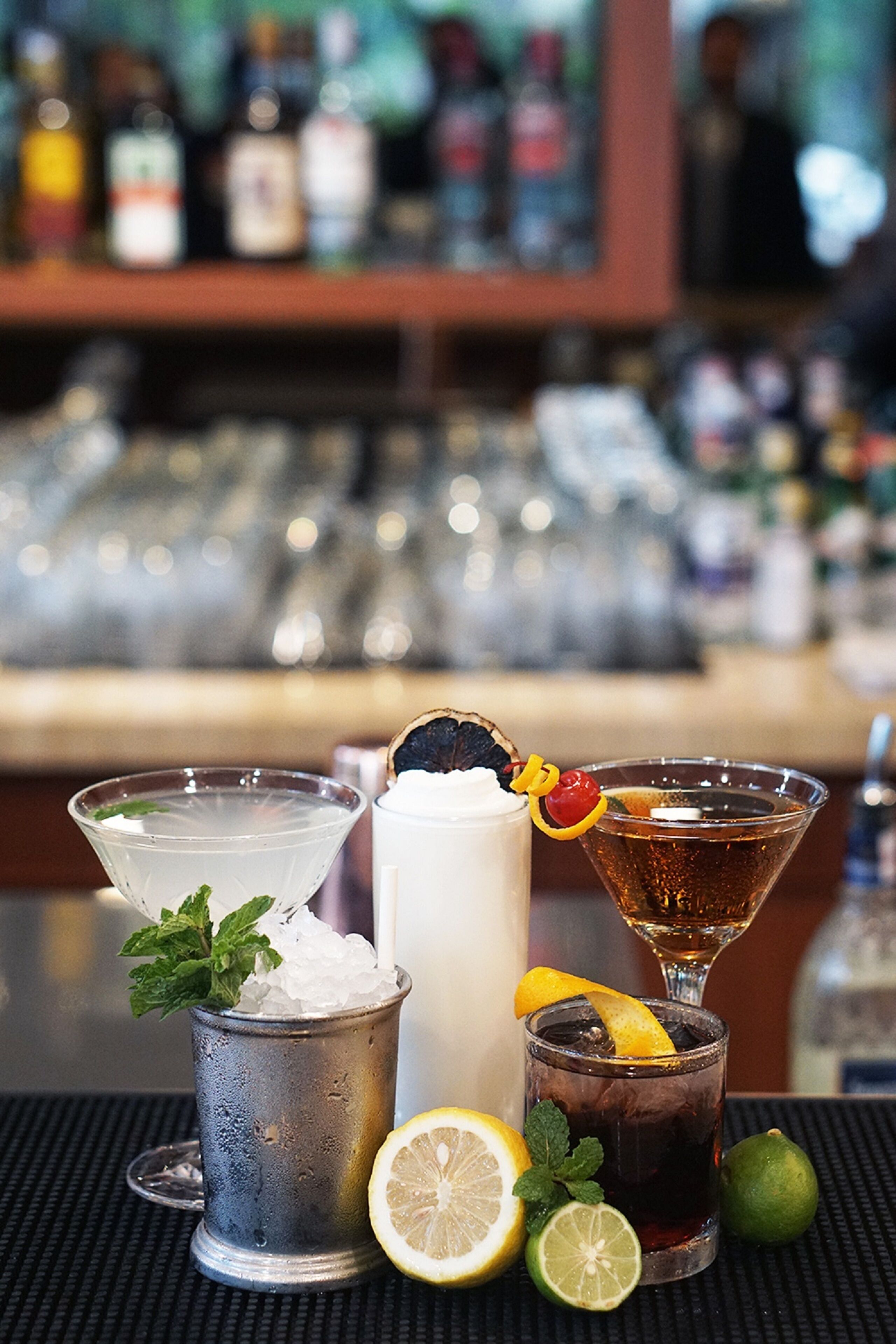 Eine Bar mit verschiedenen Getränken, darunter ein Martini, ein hohes Glas mit Eiswürfeln und ein Cocktail mit Zitronenscheibe.