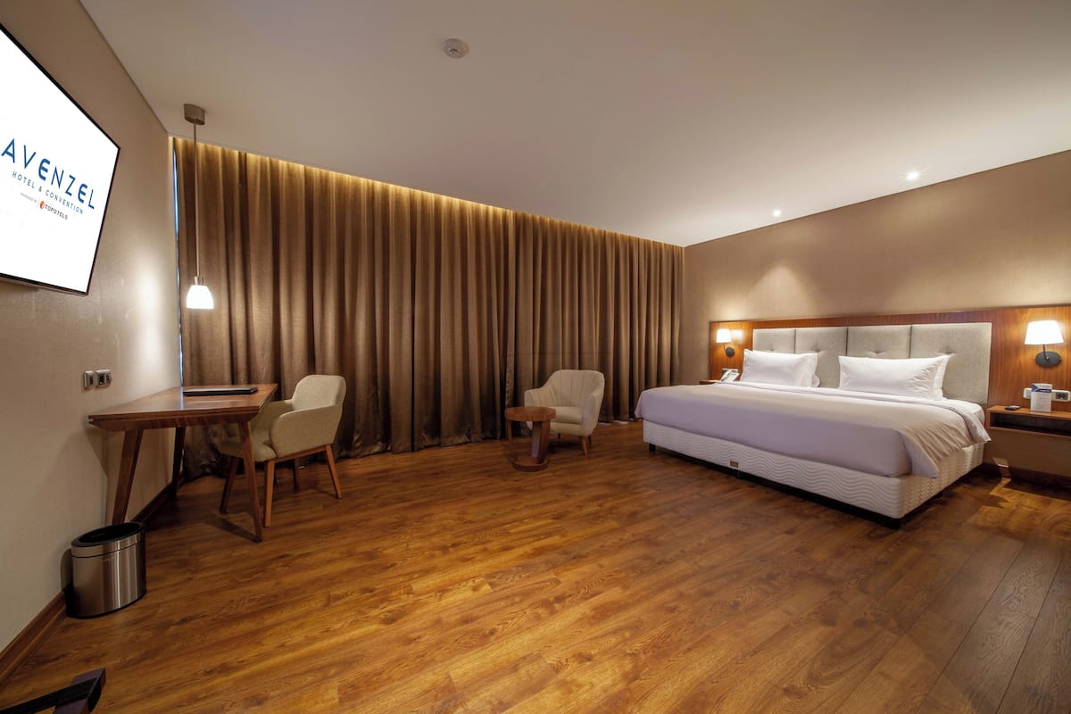 Ein Hotelzimmer mit Bett, Schreibtisch, Stuhl, Mülleimer und Fernseher an der Wand.