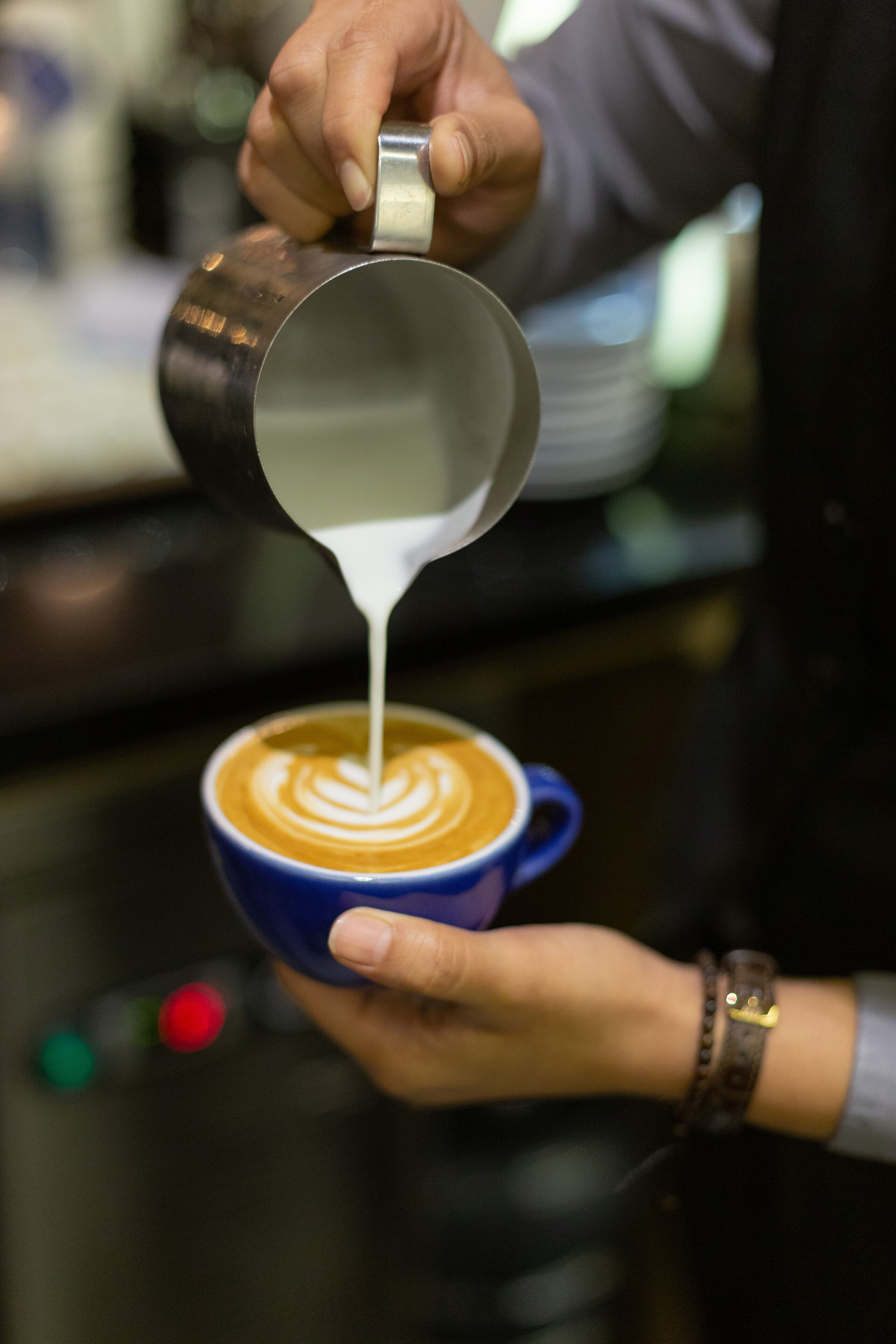 A person pouring milk into a cup of coffee, creating a latte art design.