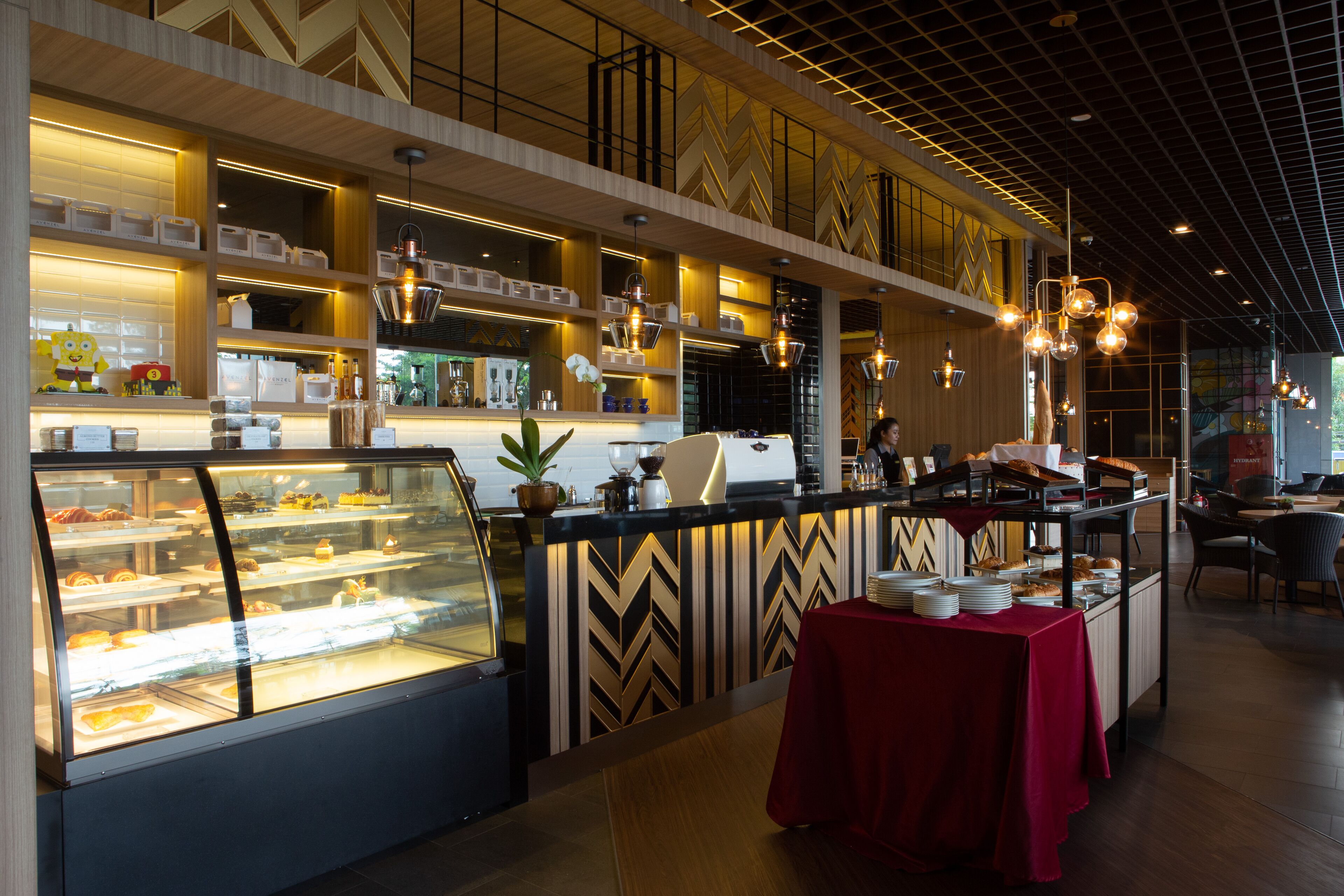 A modern cafe with a glass display case, wooden shelves, and a red tablecloth-covered table.