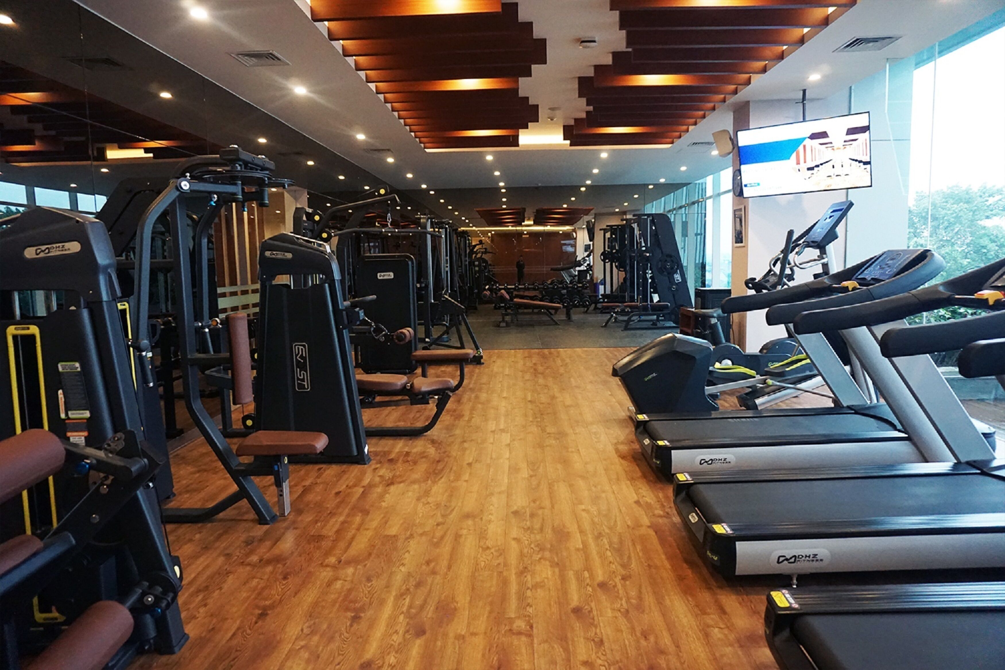 A gym with cardio machines, weight training equipment, and a large TV screen.
