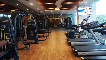 A gym with cardio machines, weight training equipment, and a large TV screen.
