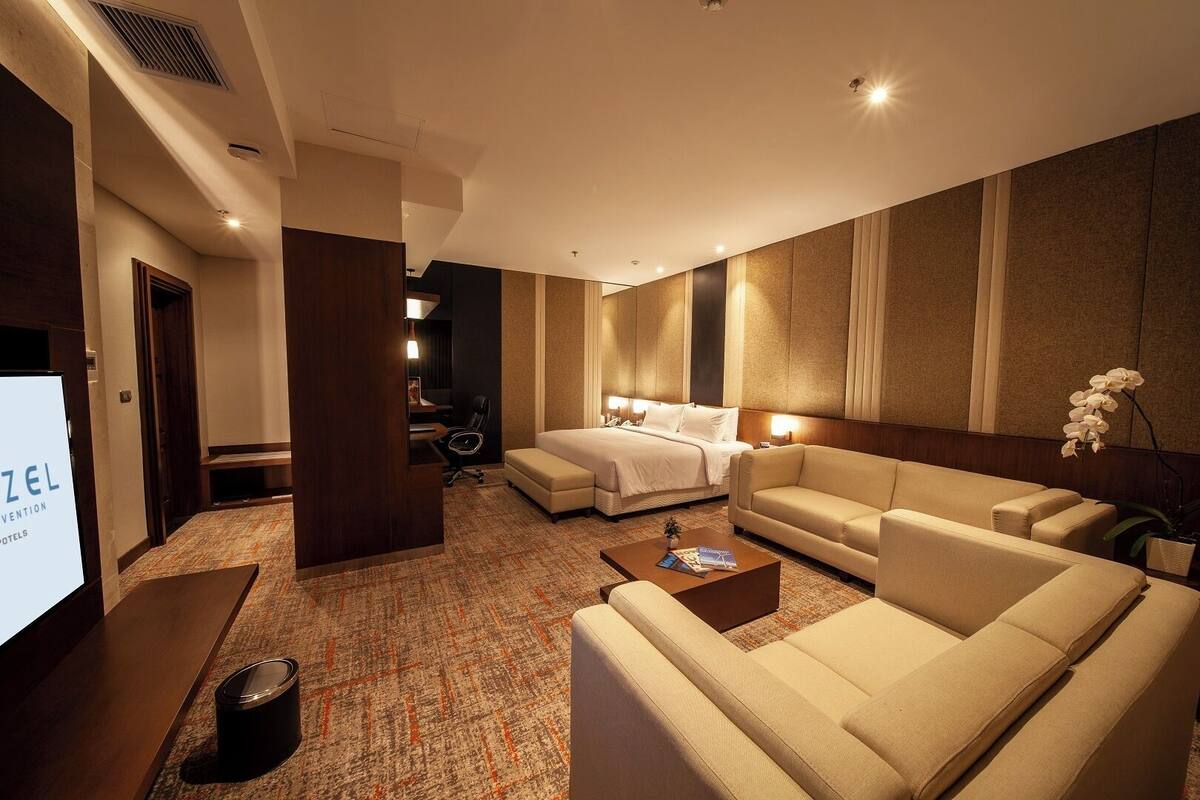 Ein Hotelzimmer mit einem Bett, einer Couch, einem Couchtisch und einem Fernseher, der "ZEL INNOVATION HOTELS" anzeigt.