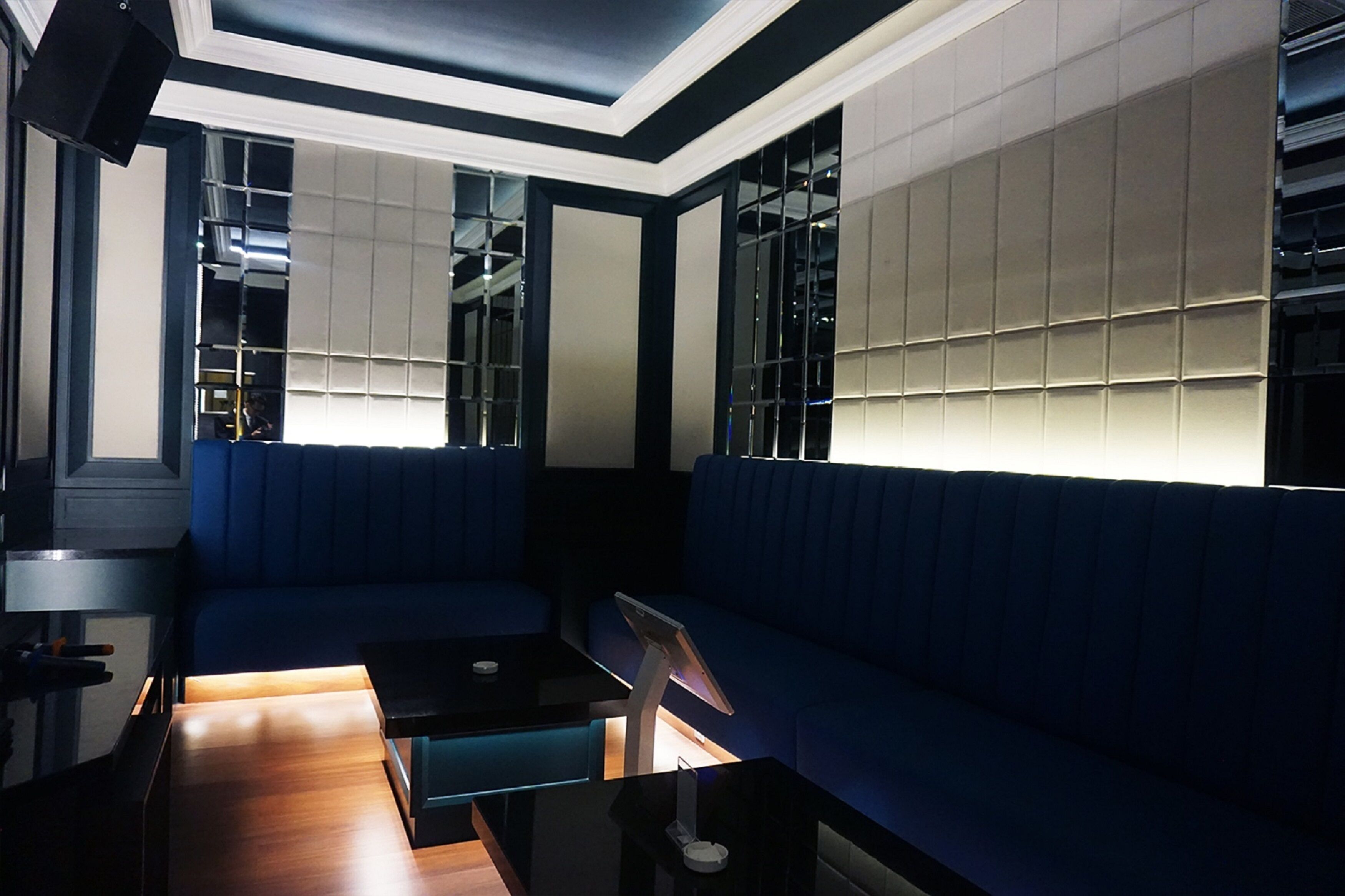 Un espace de détente moderne avec un canapé bleu, une table basse en verre et un écran numérique.