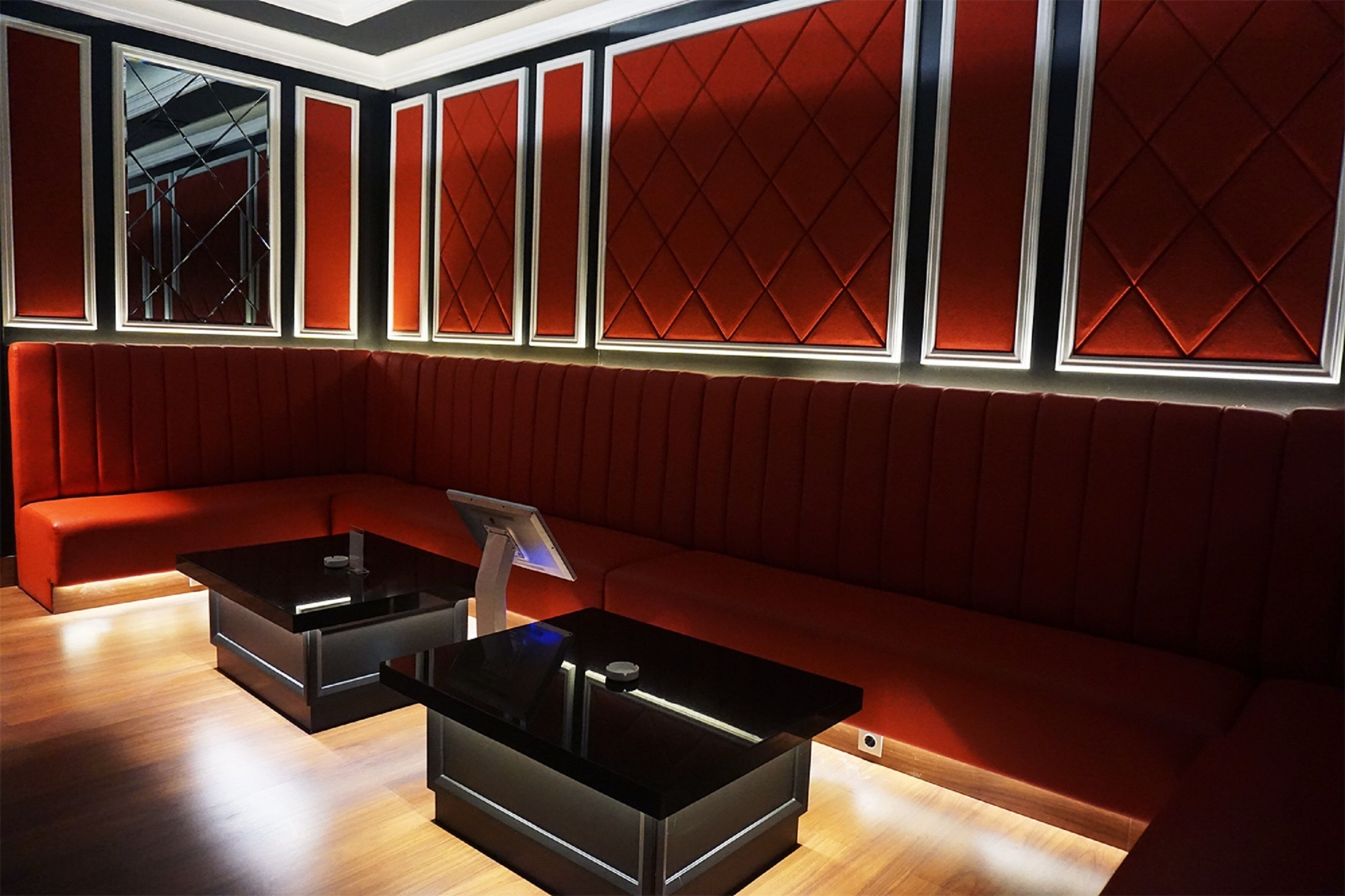 A modern lounge with a red cushioned sofa, black coffee tables, and a large window with a geometric pattern.