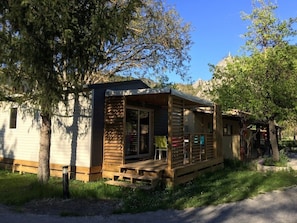 Una cabaña pequeña con terraza de madera, un porche cubierto y una mesa pequeña.