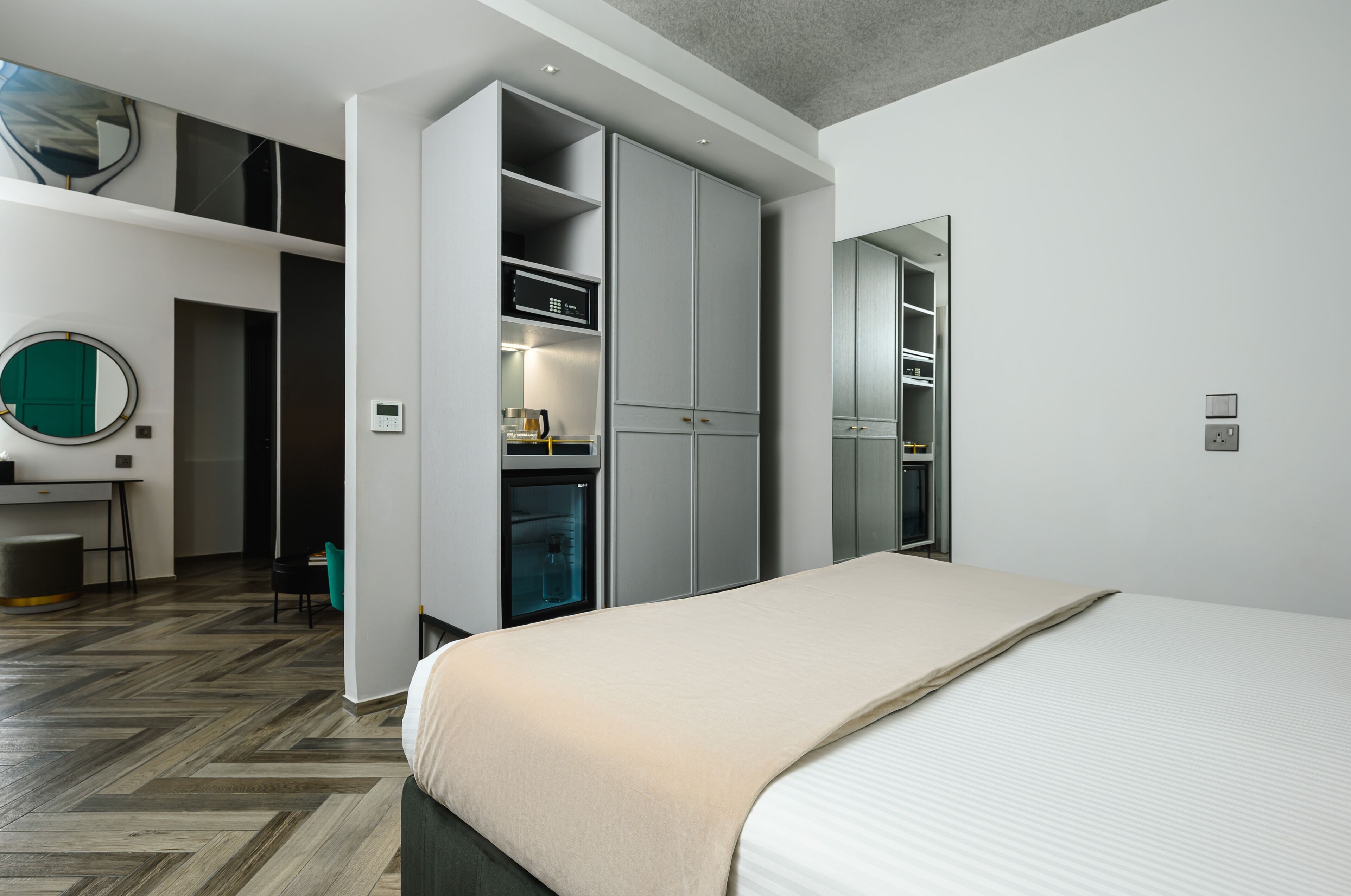A modern hotel room with a large bed, a built-in wardrobe, a desk with a chair, and a mirror.