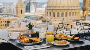 Una mesa de comedor con diversos alimentos para el desayuno y vistas panorámicas de la ciudad.