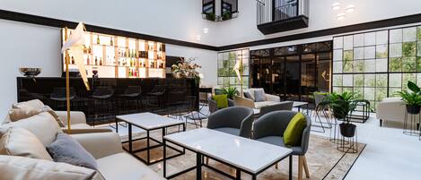 A spacious, well-lit lounge area with seating arrangements, a bar with shelves of bottles, and large windows offering views of the outdoors.
