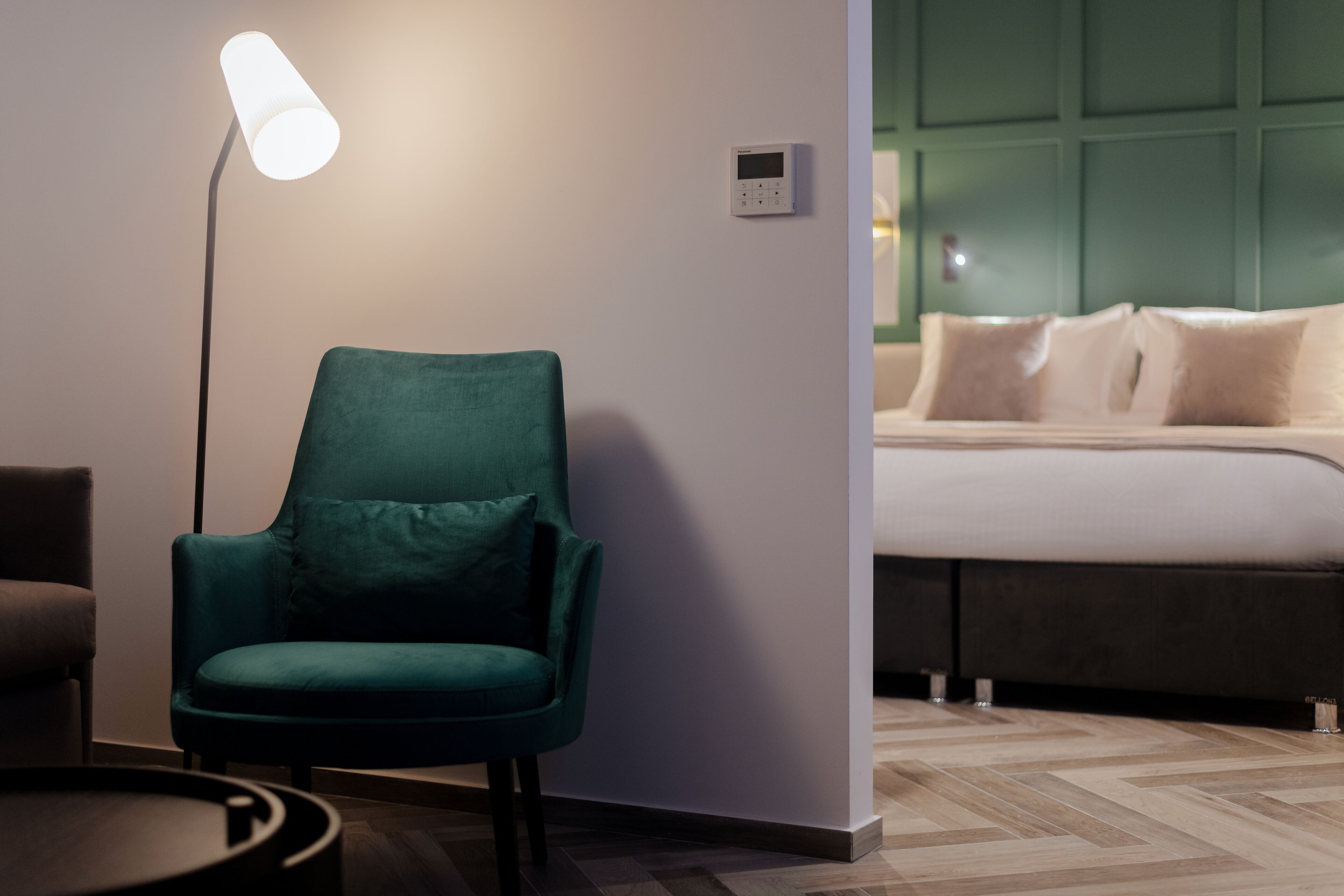 Een moderne kamer met een blauwgroene fauteuil, een vloerlamp en een bed met een groen hoofdeinde.