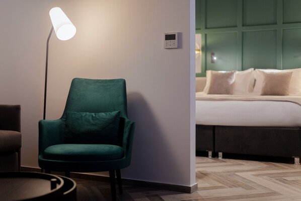 Una habitación moderna con un sillón verde azulado, una lámpara de pie y una cama con cabecera verde.