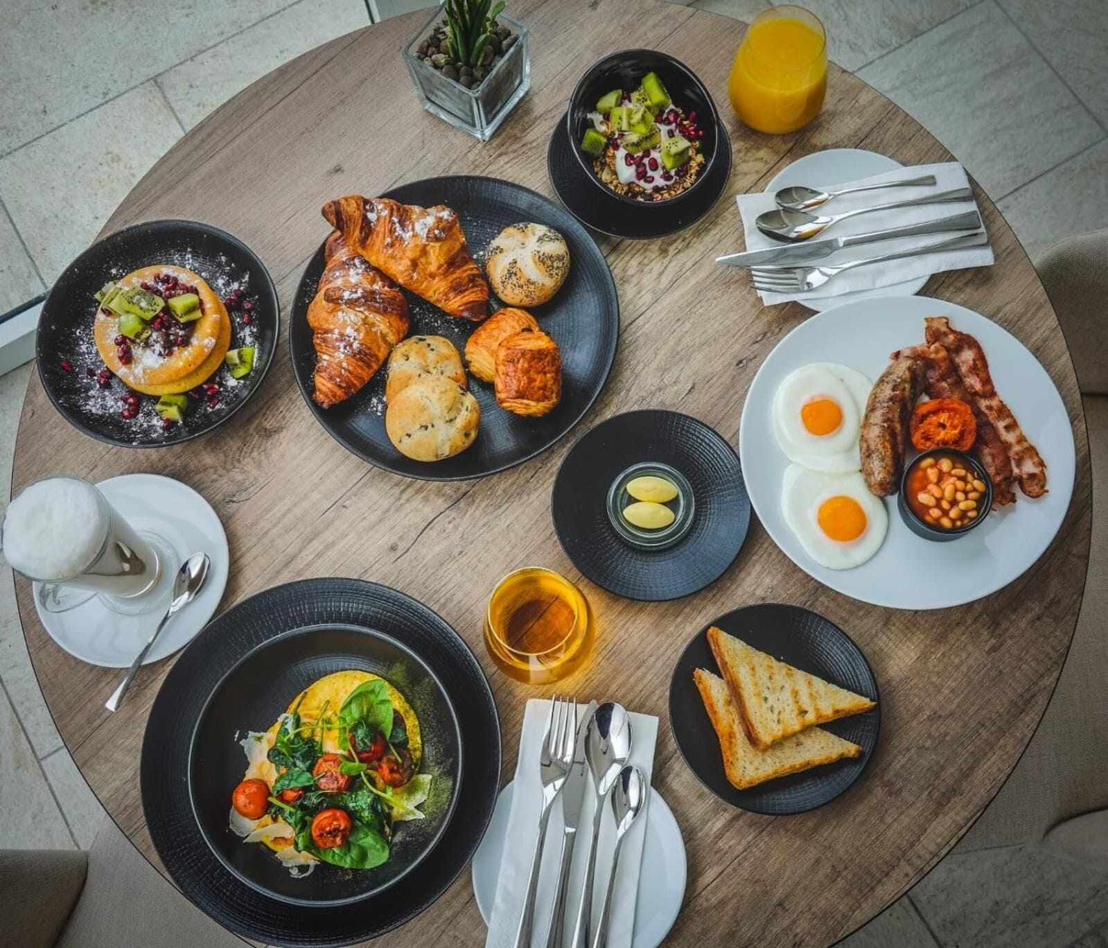 A breakfast setting with croissants, eggs, bacon, toast, and a variety of fruits and vegetables.