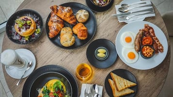 A breakfast setting with croissants, eggs, bacon, toast, and a variety of fruits and vegetables.