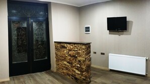 A room with a stone accent wall, a black door with glass panels, a mounted TV, and a radiator. - Cozy Hotel Kazbegi (Kazbegi)