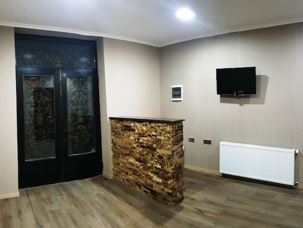 Quarto com parede de destaque em pedra, porta preta com painéis de vidro, televisão montada e radiador.