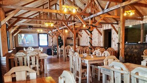 A rustic dining area with wooden tables and chairs, a stone wall, and a projector screen in the background. - Cozy Hotel Kazbegi (Kazbegi)