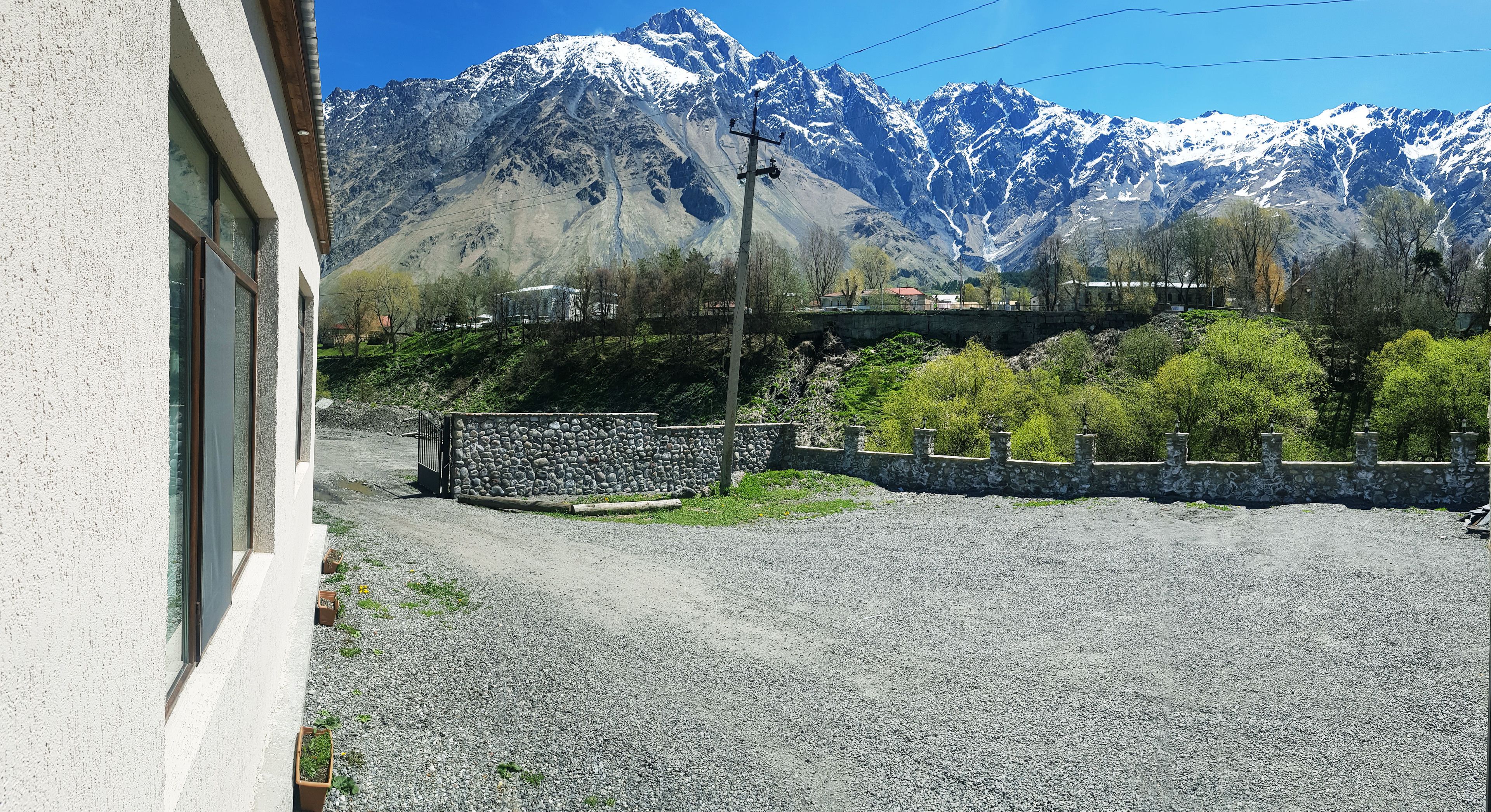 A building with a gravel driveway, a stone wall, and a view of snow-capped mountains.