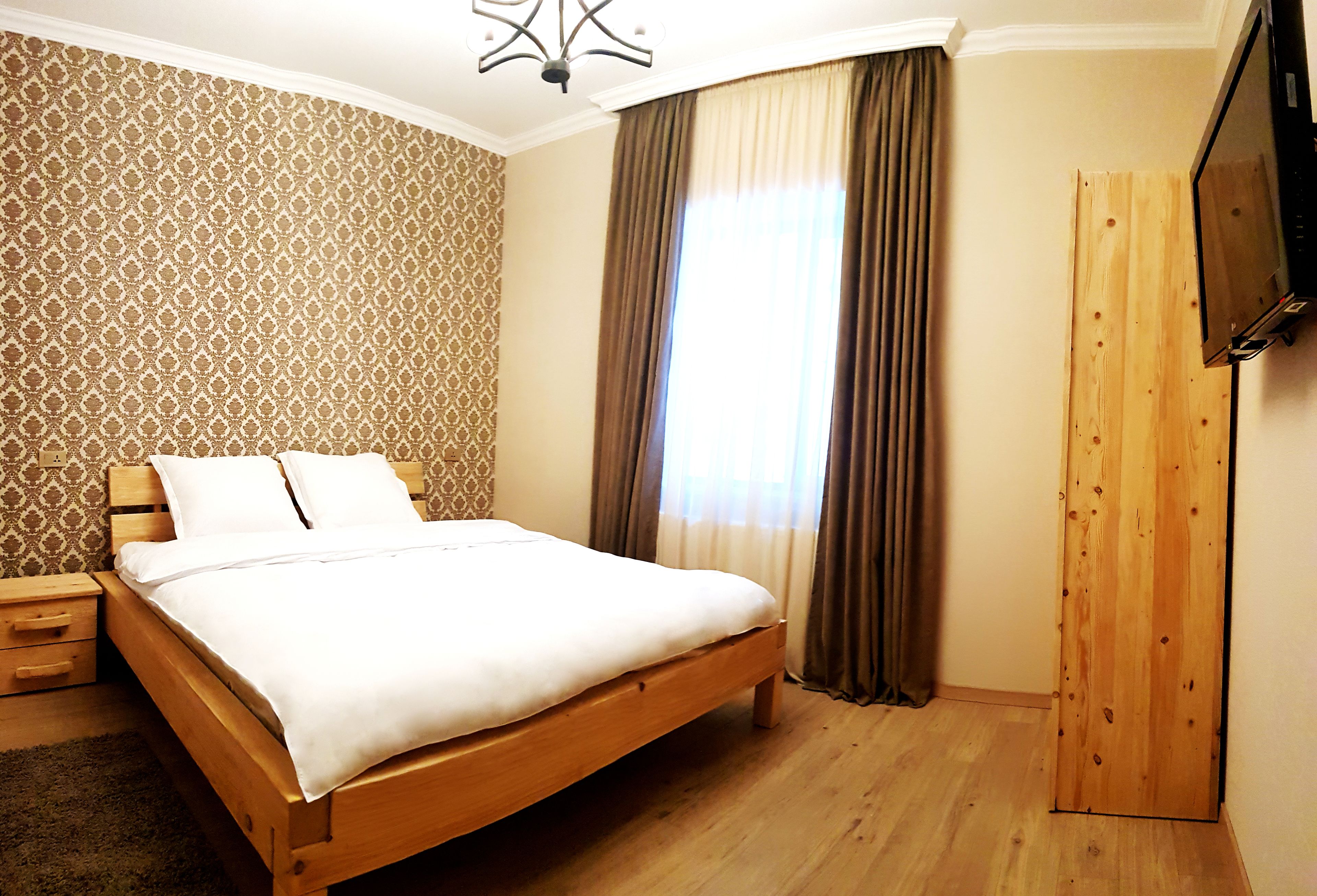 Un dormitorio con una cama de madera, una mesita de noche, un televisor montado en la pared y un armario.