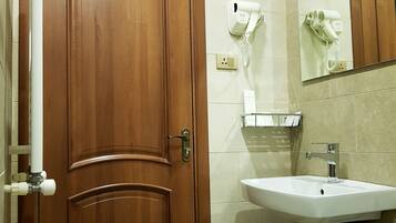 Un baño con puerta de madera, un lavabo blanco, un espejo y un secador de pelo en la pared.