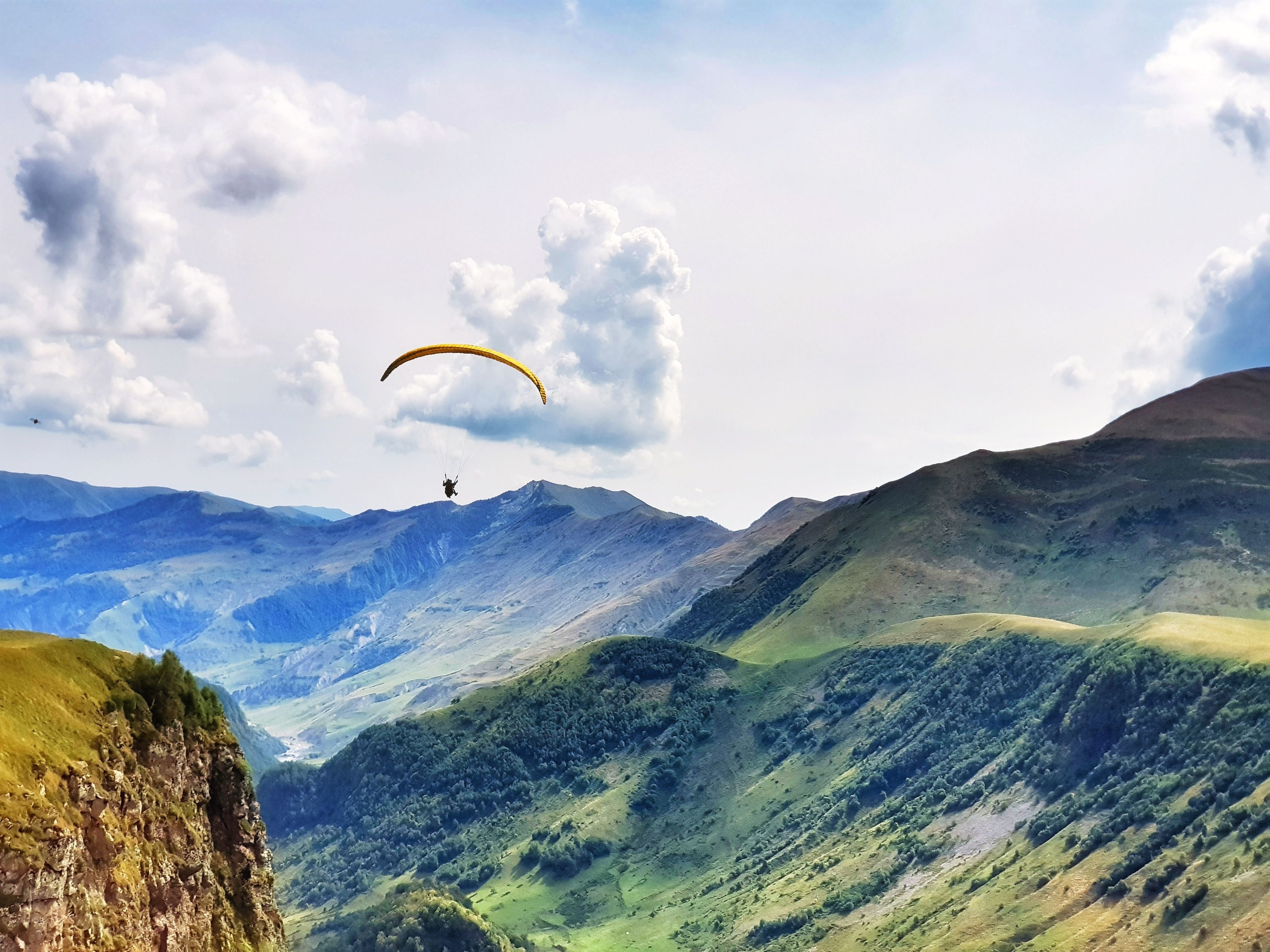 Un paisaje montañoso con un parapentista en el cielo.