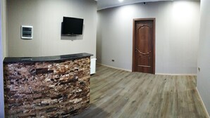 A room with a brick accent wall, a flat-screen TV mounted on the wall, and a wooden door. - Cozy Hotel Kazbegi (Kazbegi)