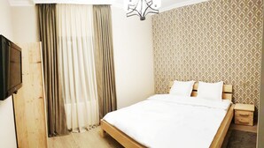 A bedroom with a wooden bed, a TV on the left, and a patterned wall. - Cozy Hotel Kazbegi (Kazbegi)