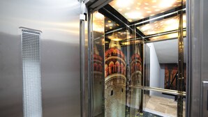 Ascensor con puerta de cristal, rejilla metálica y reflejo de un edificio con torres.