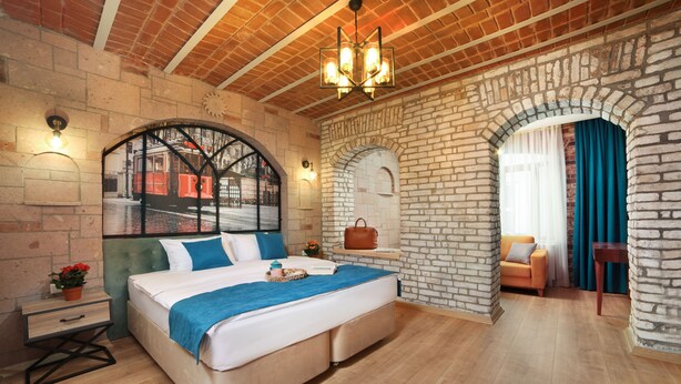 Un dormitorio con una cama grande, una mesita de noche, un aparador y una ventana que da a una vista de un tranvía, junto a una pared de ladrillo.