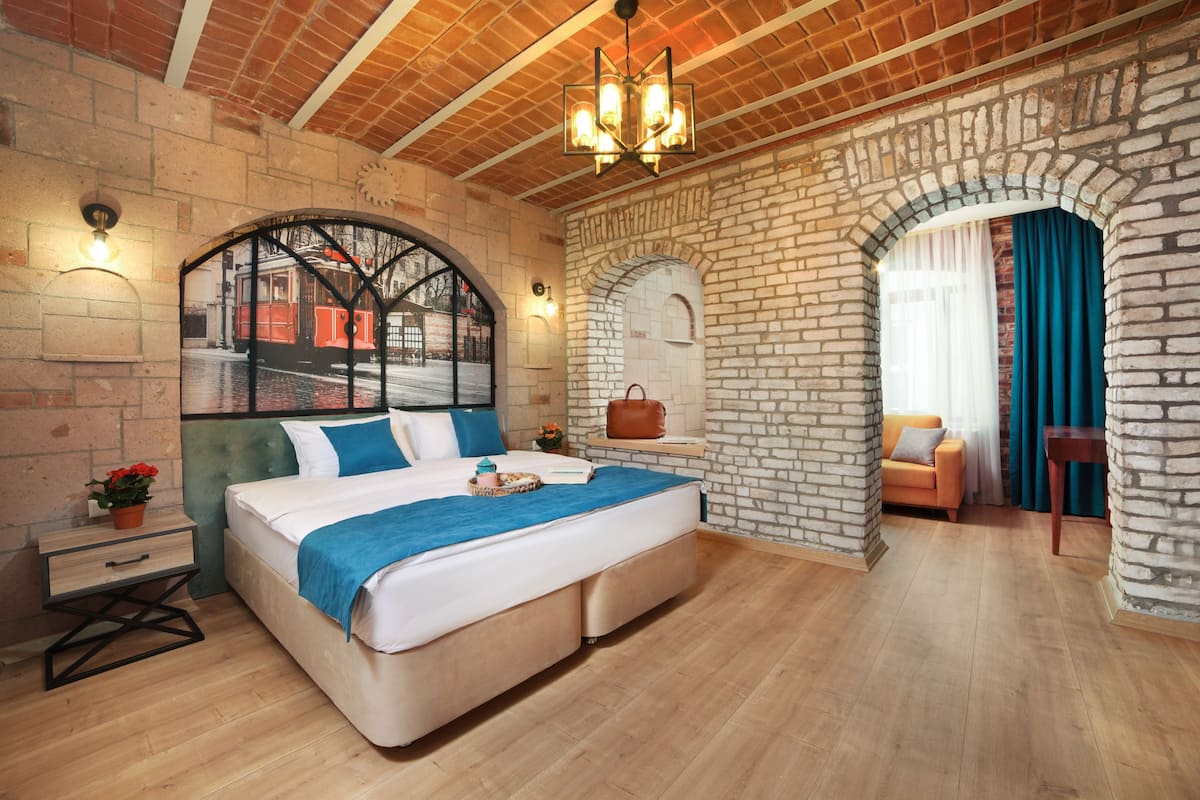 Un dormitorio con una cama grande, una mesita de noche, un aparador y una ventana que da a una vista de un tranvía, junto a una pared de ladrillo.