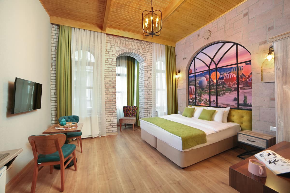 Una habitación de hotel con una cama grande, un escritorio con silla, un televisor y un mural en la pared.