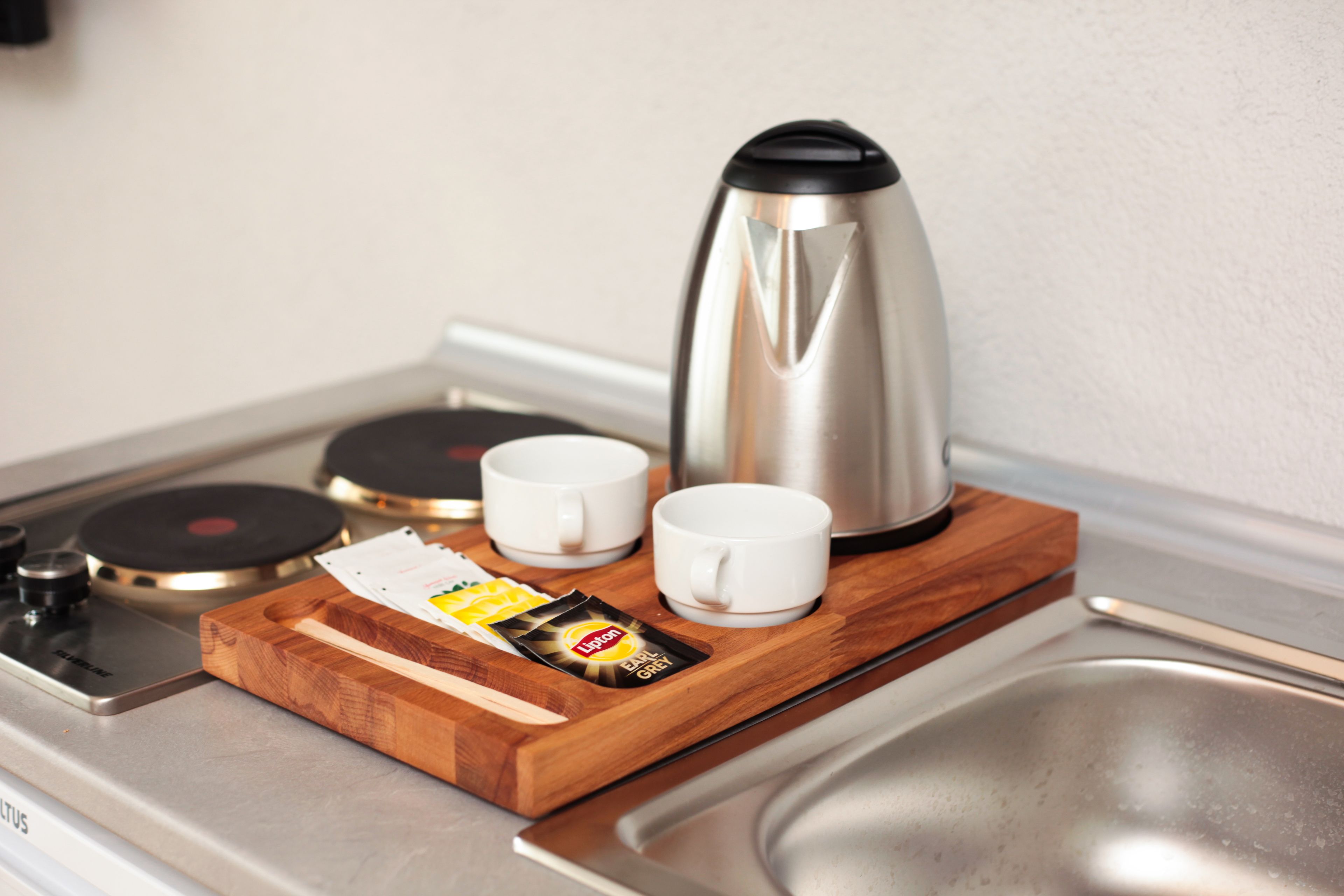 A kitchen counter with a coffee maker, two white cups, a wooden tray, and a packet of sugar.