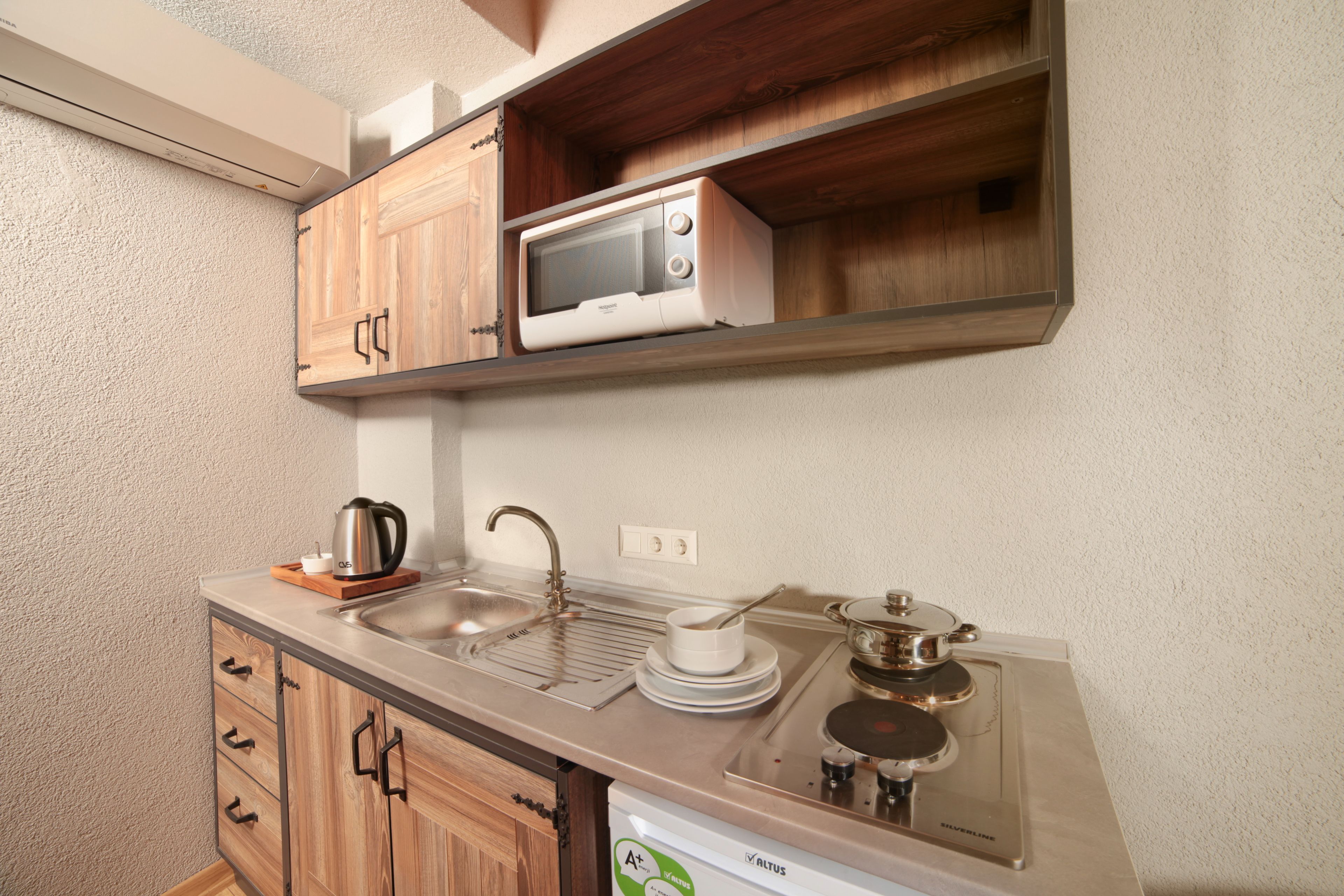 Cocina compacta con armarios de madera, microondas, fregadero y estufa integrada.