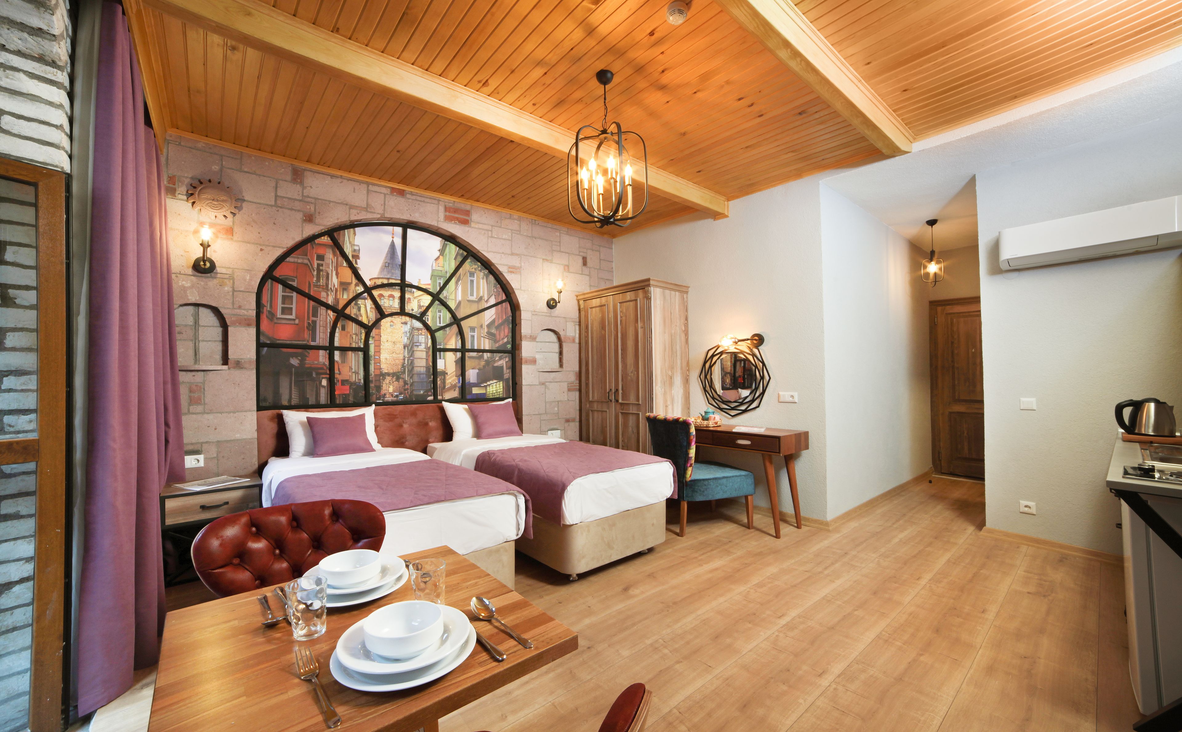 Una habitación acogedora con dos camas, una mesa de comedor con platos y cubiertos, techo de madera y pared de ladrillo con vista a la ventana.